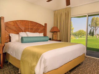 Spacious bedroom with a large bed, wooden headboard, and a sliding glass door opening to a golf course view