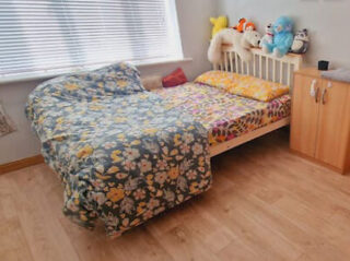 A bedroom with a floral bedspread, a wooden headboard, and a collection of plush toys on a shelf