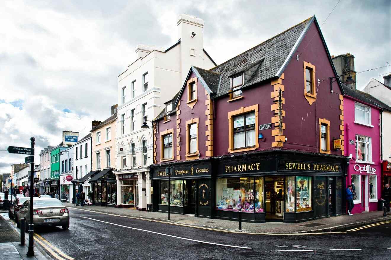 Picturesque town corner in Killarney featuring a pharmacy and other shops, with multi-colored facades under a dynamic cloudy sky