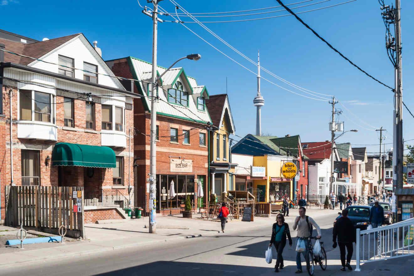 A sunny street scene in Toronto’s Annex neighborhood, with the CN Tower in the distance, and locals walking past colorful storefronts