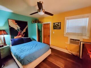 Eclectic bedroom with a bright blue bedspread, large guitar art piece on the wall, and a Beatles picture