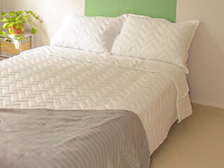 Simple yet elegant bedroom with a textured white comforter and matching pillows, accented by a green headboard