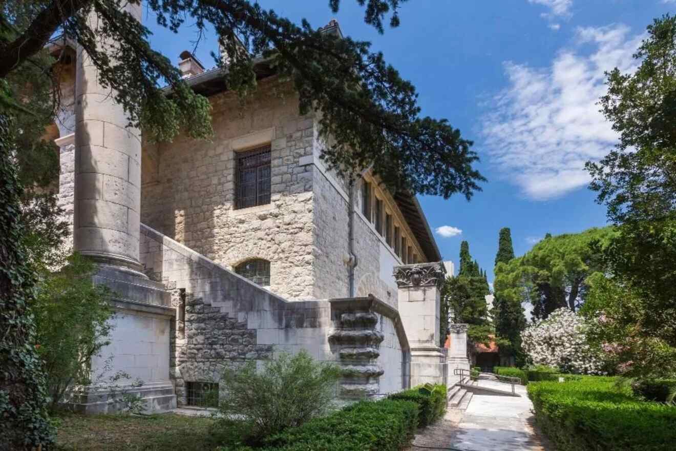 Elegant historical villa in Split, Croatia, surrounded by lush Mediterranean gardens under a bright blue sky with white clouds