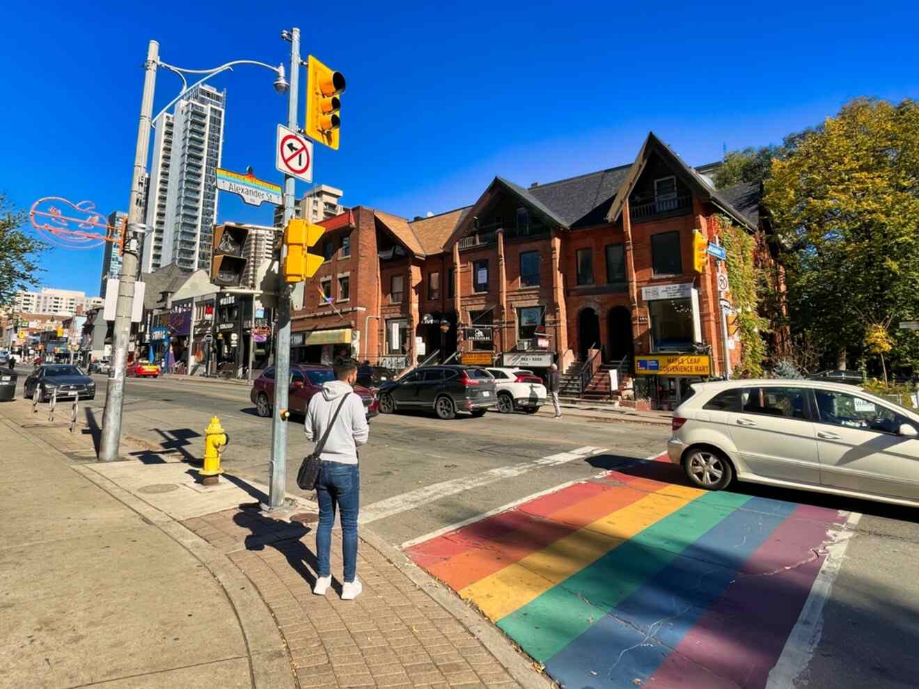 A pedestrian crossing a rainbow-colored crosswalk in Toronto's The Village, reflecting the area’s recognition as a monument to gay culture