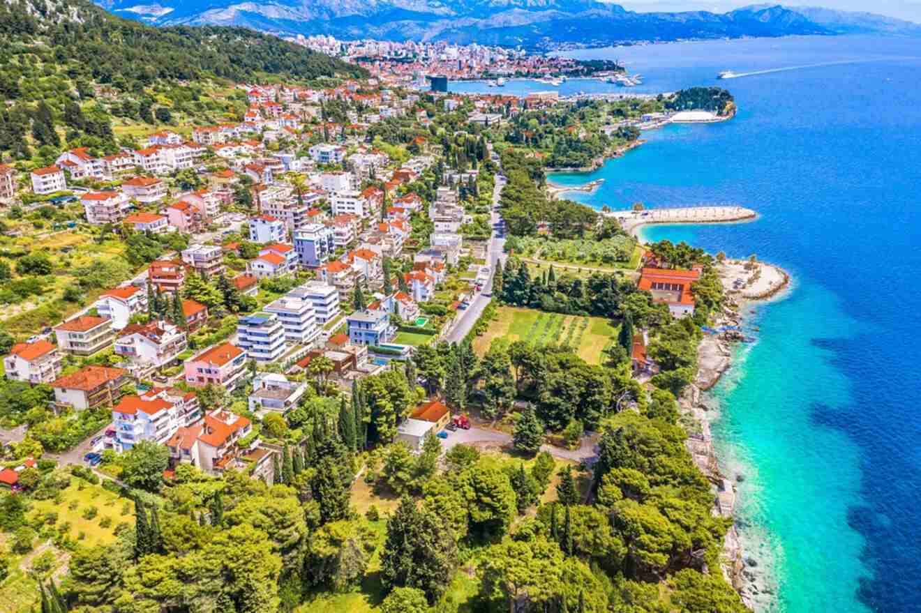 A vibrant aerial shot of coastal residential areas outside Split, with houses densely packed on lush greenery, leading up to the clear blue waters of the Adriatic Sea