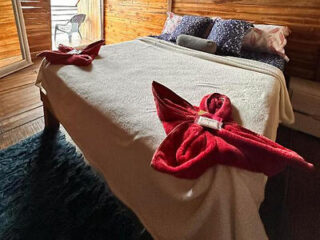 Inviting massage table with red towel swans and a welcoming note, set in a room with warm wood tones and soft lighting