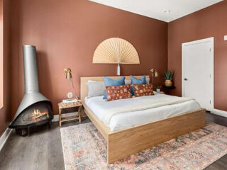 Cozy bedroom featuring a wood-frame bed, a freestanding fireplace, accented with warm and earthy tones