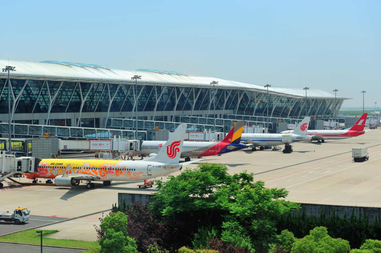 A view of the tarmac at Shanghai Pudong International Airport, with various airline planes docked at the gates under a modern glass terminal
