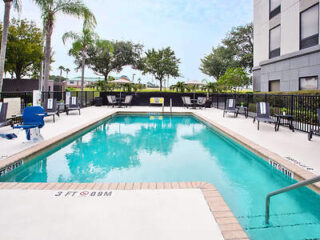 Hotel poolside area featuring patio furniture, a clear blue pool, and a well-maintained deck under a bright sky