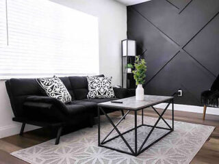 Modern living room with a black geometric accent wall, leather sofa, and minimalist furnishings