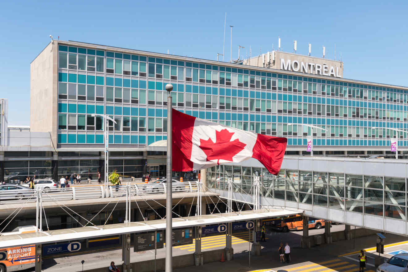 The Canadian flag fluttering in front of the Montreal airport terminal, with travelers and transport in the foreground