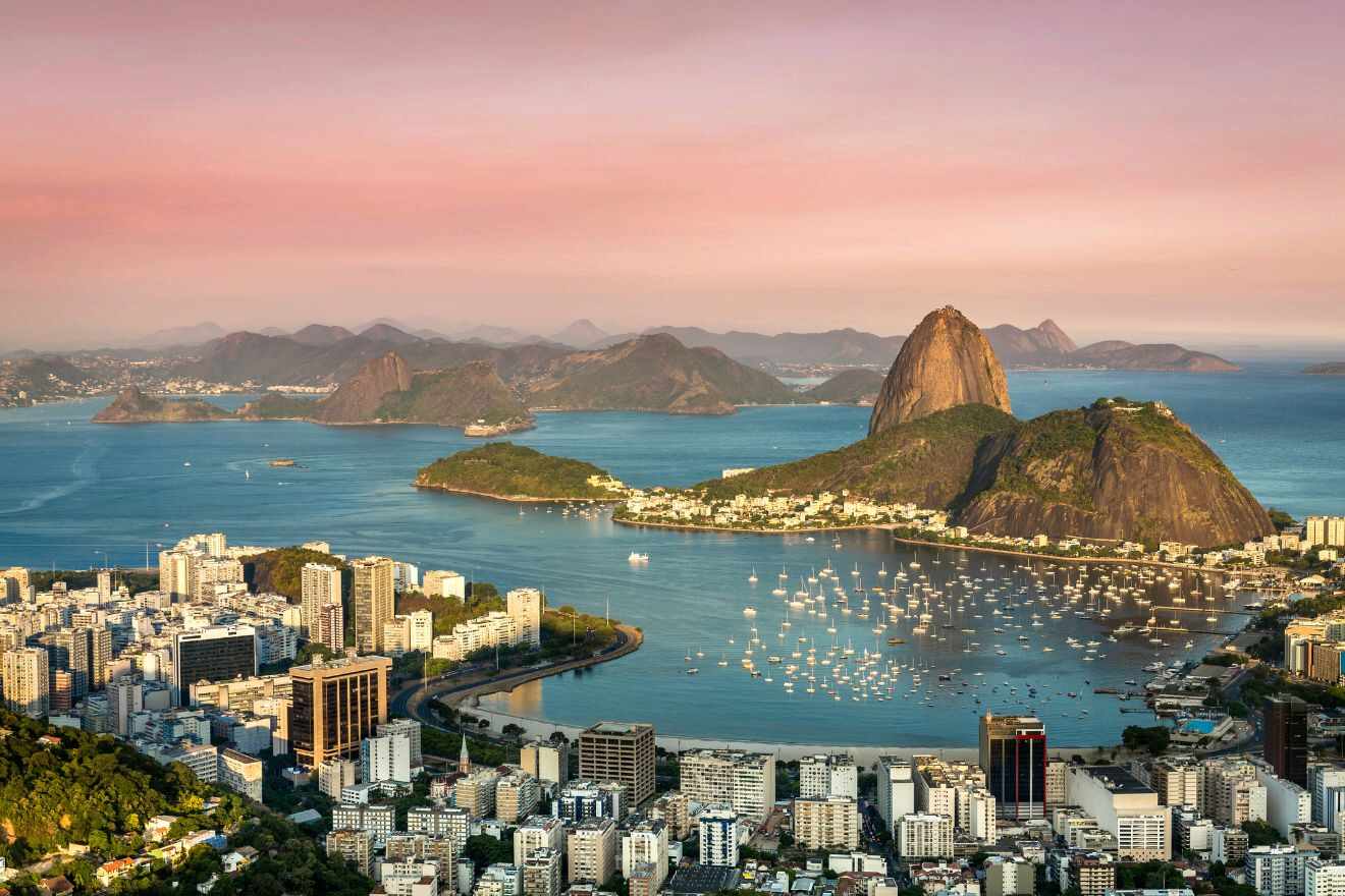 Aerial view of Rio de Janeiro's bay with Sugarloaf Mountain prominent at dusk, the city's lights beginning to twinkle