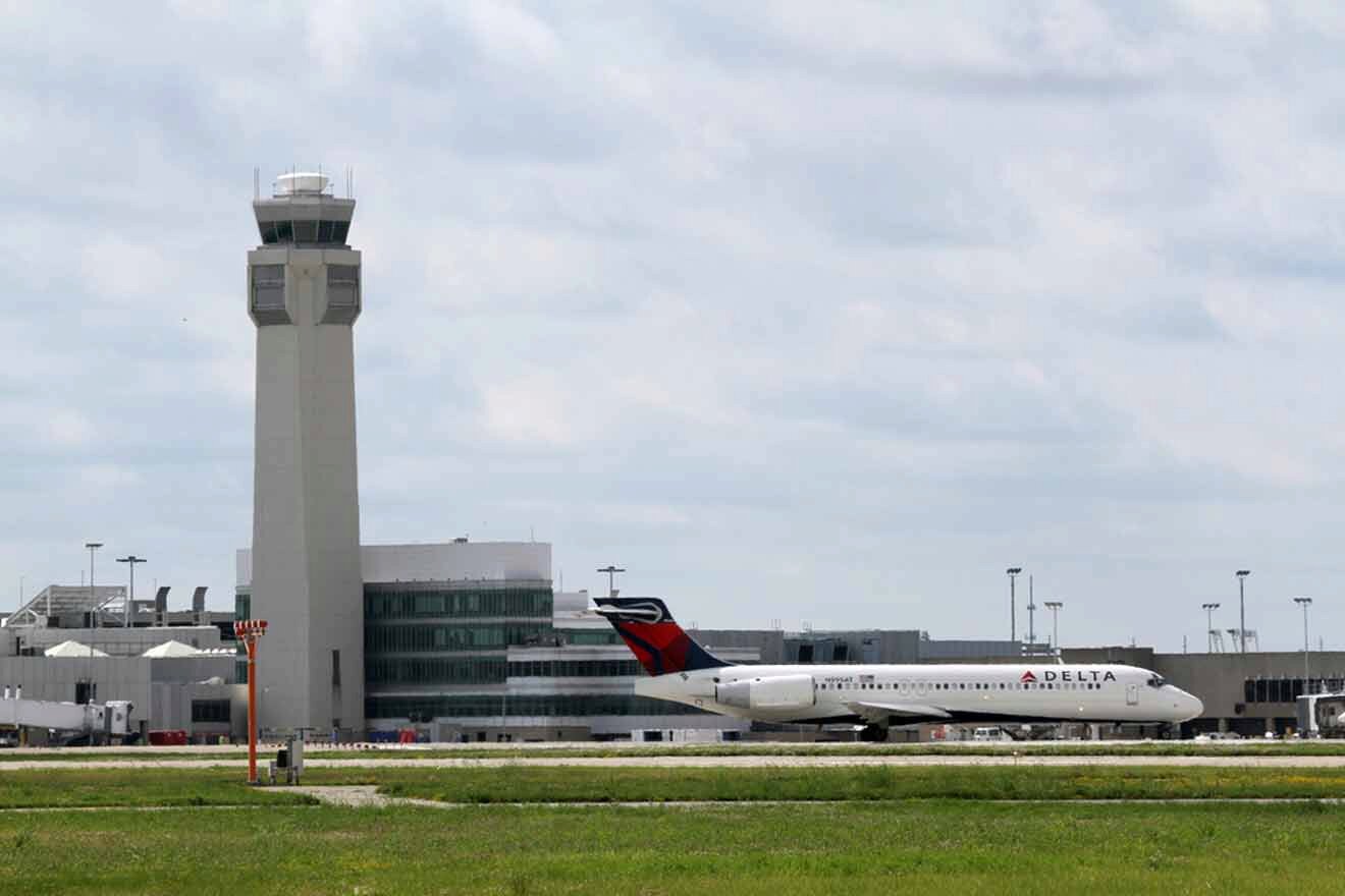 The control tower and a Delta airplane on the tarmac at an airport, with the terminal buildings in the background.