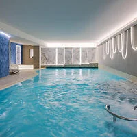Indoor swimming pool with blue water, white lounge chairs on the left, and modern lighting fixtures on the right wall.