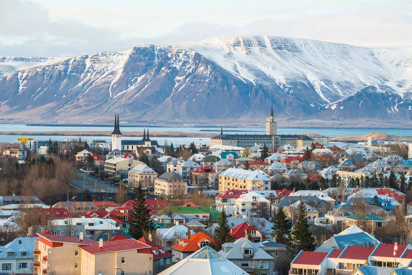 Panoramic view of Reykjavik with colorful rooftops, prominent church spires, and a backdrop of snow-capped mountains under a clear blue sky