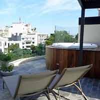 A rooftop relaxation area with a wooden hot tub and comfortable lounge chairs, boasting views of the cityscape.