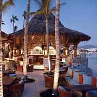 Thatched-roof beachfront bar at dusk with palm trees and ambient lighting creating a welcoming tropical atmosphere.