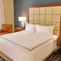 Cozy hotel room featuring a large bed with an oversized headboard, crisp white linens, and ambient lighting.