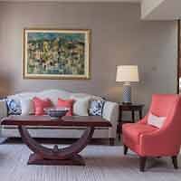 Elegant hotel living room with a large painting above a sofa, a wooden coffee table, and a vibrant red armchair.