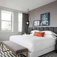 A chic and well-lit hotel room with a large bed, a striking black and white striped rug, and modern artwork adding a touch of color.