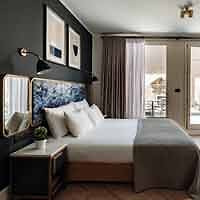 A cozy boutique hotel bedroom with a queen-sized bed, dark walls, and modern furnishings.