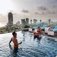 People enjoying a rooftop swimming pool with a city skyline backdrop, showcasing a vibrant urban resort setting.