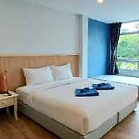 Simplistic and neat hotel bedroom with a large comfortable bed, a small bedside table, and a pop of blue from the curtains, offering a peaceful retreat for travelers.