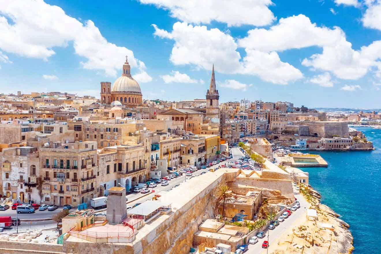 Aerial view of Valletta, Malta, showcasing the historic architecture with the prominent St. Paul's Pro-Cathedral and Carmelite Church domes against a backdrop of the Mediterranean Sea under a clear blue sky.