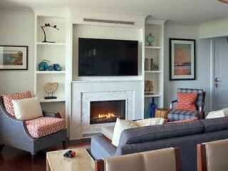Contemporary living room with a fireplace, wall-mounted TV, patterned armchairs, and neutral-toned sofa, creating a comfortable, modern space