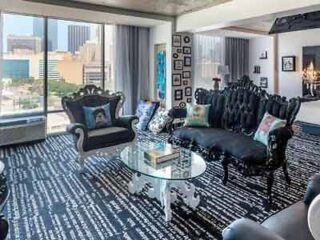 Eclectic living room in a high-rise hotel with bold black furniture, patterned carpet, and a view of the Dallas skyline.