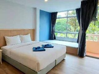 A bright and airy hotel room with a large bed, clean white bedding, and contrasting blue curtains, offering a view of lush greenery outside, symbolizing a comfortable stay in a tropical setting.