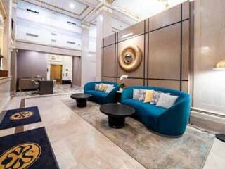 A modern hotel lobby with luxurious blue sofas, a bold golden art piece on the wall, and a marble floor that exudes opulence.