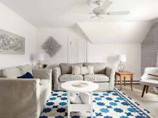 Airy and bright living room with a coastal theme, featuring a soft sofa, decorative wall art, and a bold blue and white patterned rug.