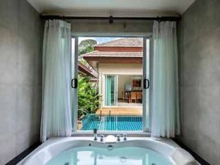 A luxurious bathtub with a view of a private pool and tropical villa, framed by sheer curtains, creating an indulgent and relaxing bathing experience.