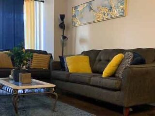 Comfortable living area with a gray sectional sofa, decorative yellow pillows, and a vintage coffee table, offering a homely feel.