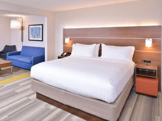Modern and inviting hotel room in Holiday Inn Express with a plush king-sized bed, blue sleeper sofa, and warm lighting