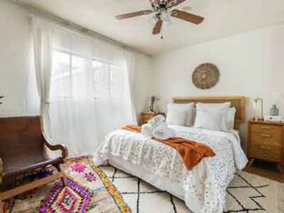 A quaint bedroom with a vintage aesthetic, featuring lace bedding, a colorful rug, and a wooden rocking chair.