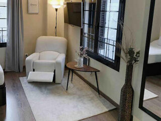 Elegant sitting area with a plush white armchair, round wooden table, and chic floor lamp beside a large mirror