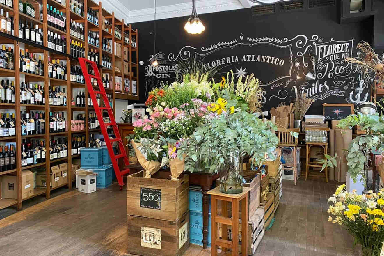 A charming and rustic interior of Florería Atlántico, featuring wall-to-wall shelves filled with an assortment of wine bottles, a vibrant display of flowers for sale, and an antique-looking blackboard with artistic chalk inscriptions is hiding a speakeasy in buenos aires.