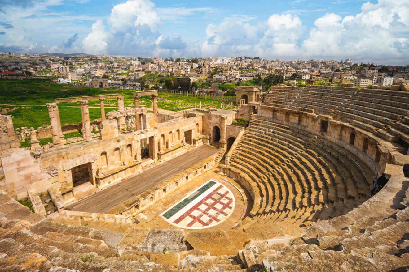 A panoramic view of the ancient Roman Theater in Amman, Jordan, showcasing the historic architecture with rows of stone seats and a stage set against a modern city backdrop