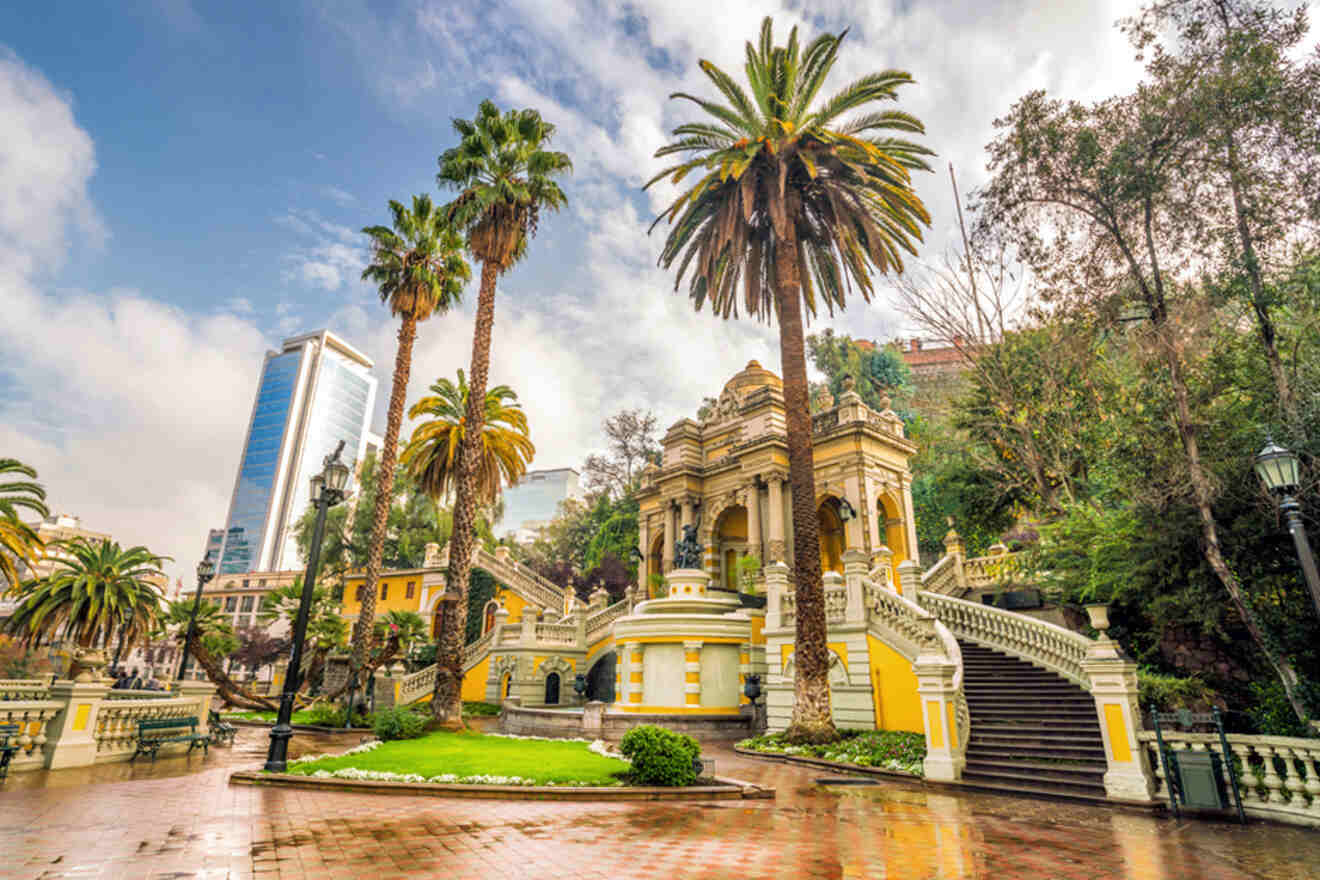 Fountain at Santa Lucia Hill with a neoclassical yellow and white structure, tall palm trees, and modern glass buildings in the background, Santiago, Chile