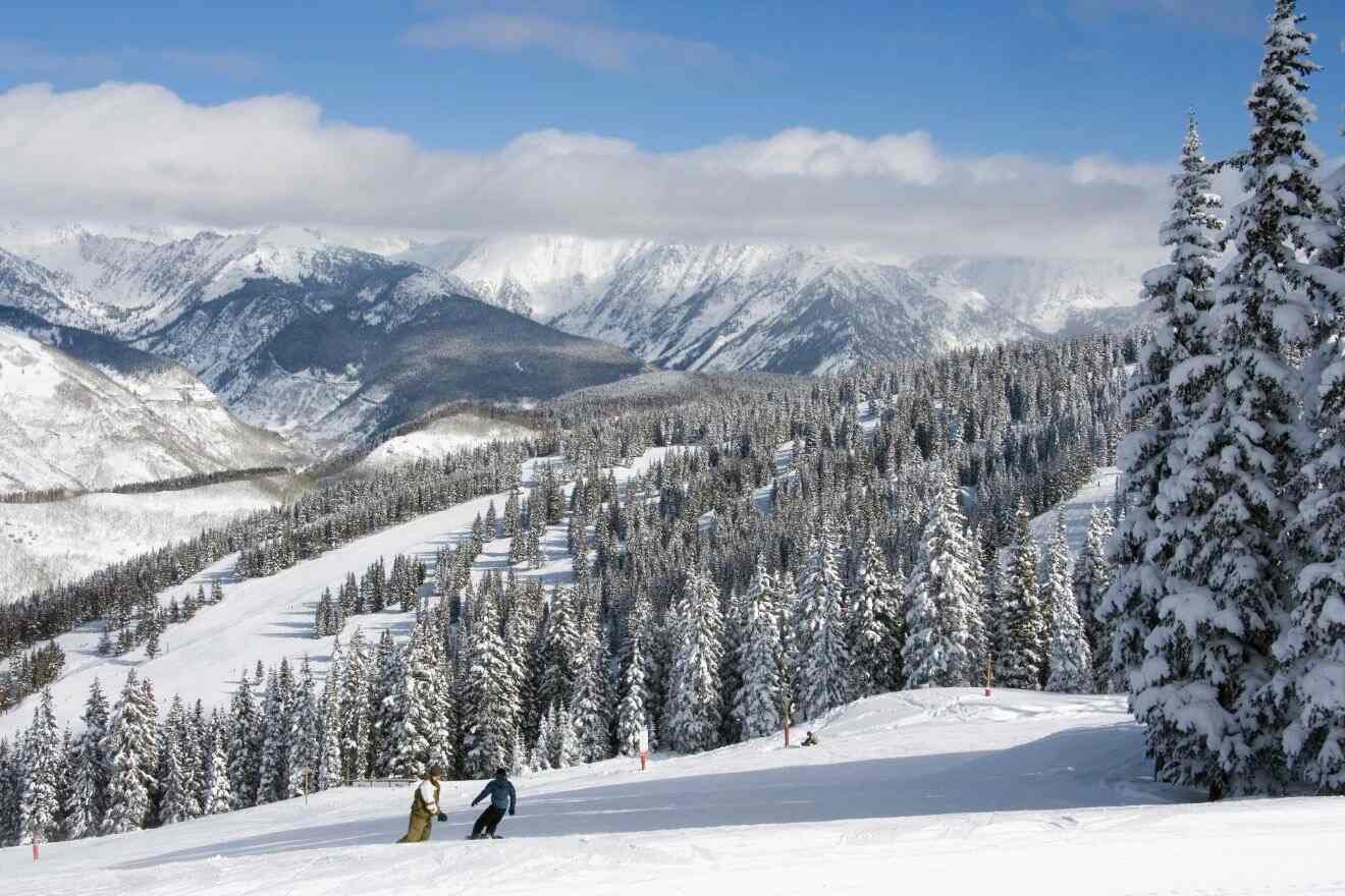 Two skiers descending a pristine snowy trail in Vail with a backdrop of majestic snow-capped mountains and pine forests