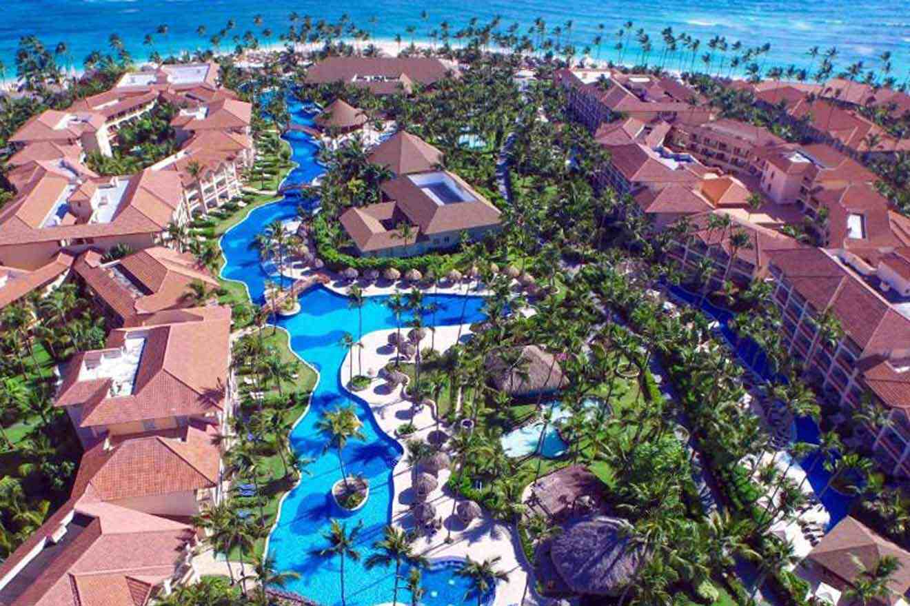 Overhead view of the Majestic Colonial resort in Punta Cana, highlighting its sprawling swimming pools, red-tiled roofs, and lush palm tree landscaping, with the ocean in the backdrop.