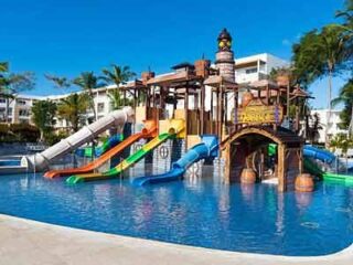 Water park area with colorful slides and a pirate-themed play structure at Princess Family Club Bavaro, under a clear blue sky.