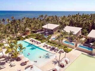 Aerial view of Catalonia Royal Bavaro resort with swimming pools surrounded by palm trees and beachside cabanas.
