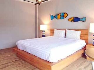 Bright and welcoming bedroom with a large comfortable bed, colorful fish artwork on the wall, and minimalist decor, creating a cheerful and relaxing environment.