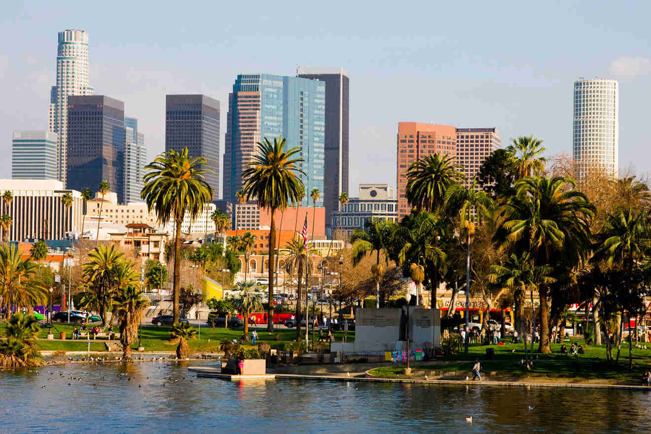 Scenic view of Downtown Los Angeles with a foreground of lush palms in a park by a lake, reflecting a blend of nature and urban architecture.