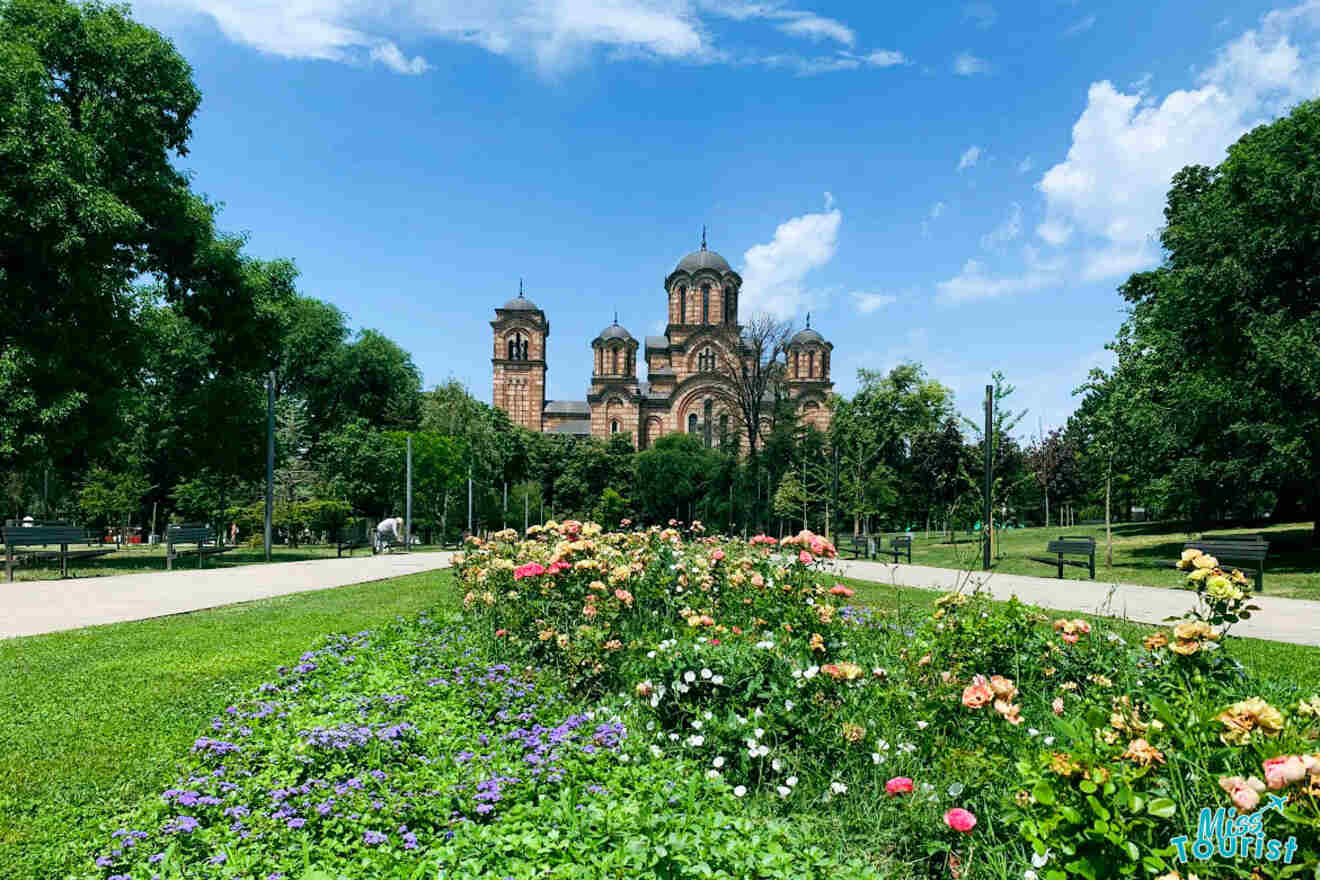 St. Mark's Church in Belgrade, surrounded by lush greenery and vibrant flowerbeds under a clear blue sky, exemplifying the city's historical and natural beauty