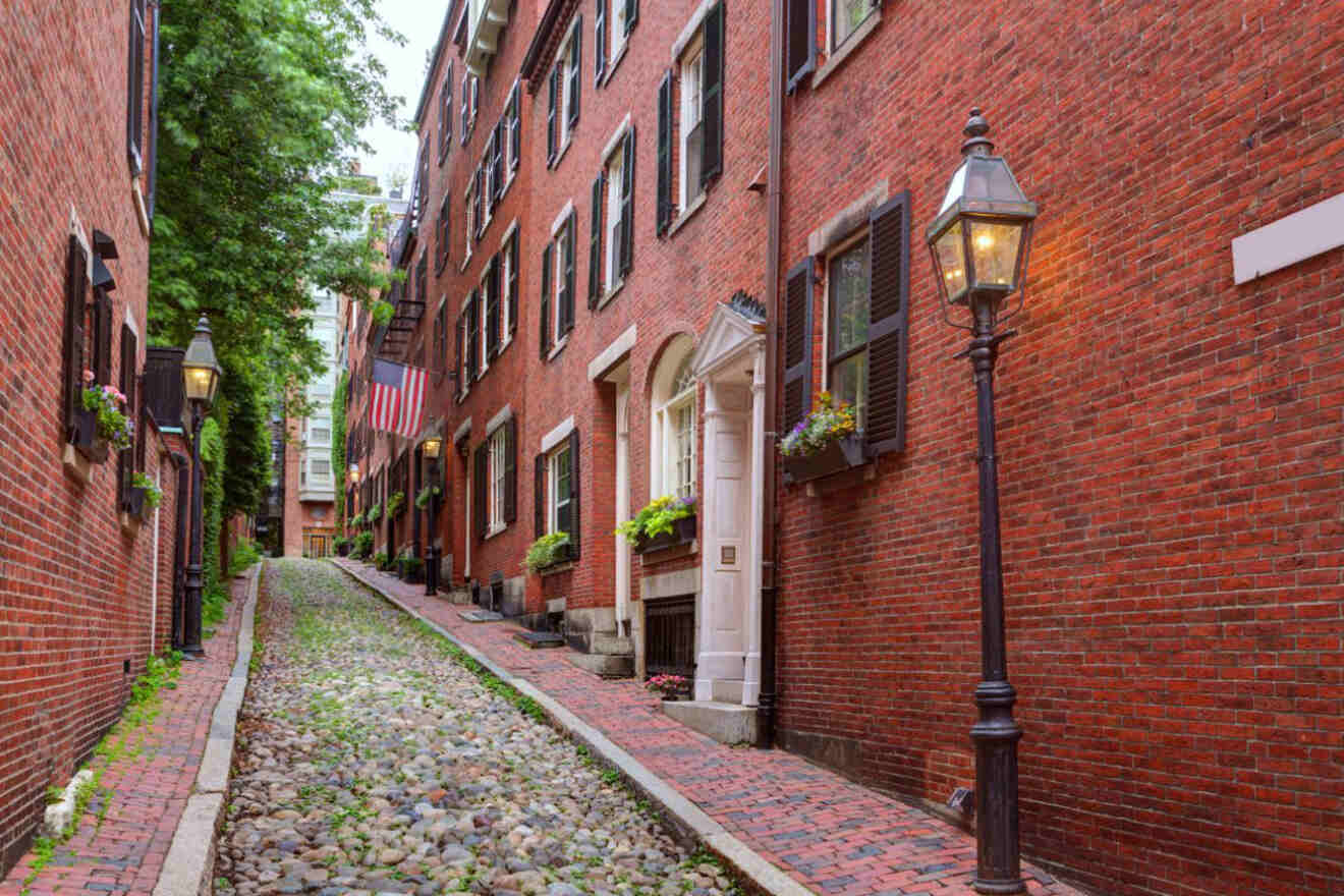 The historic Acorn Street in Beacon Hill, Boston, characterized by its cobblestone road, brick rowhouses with American flags, and gas-style streetlamps