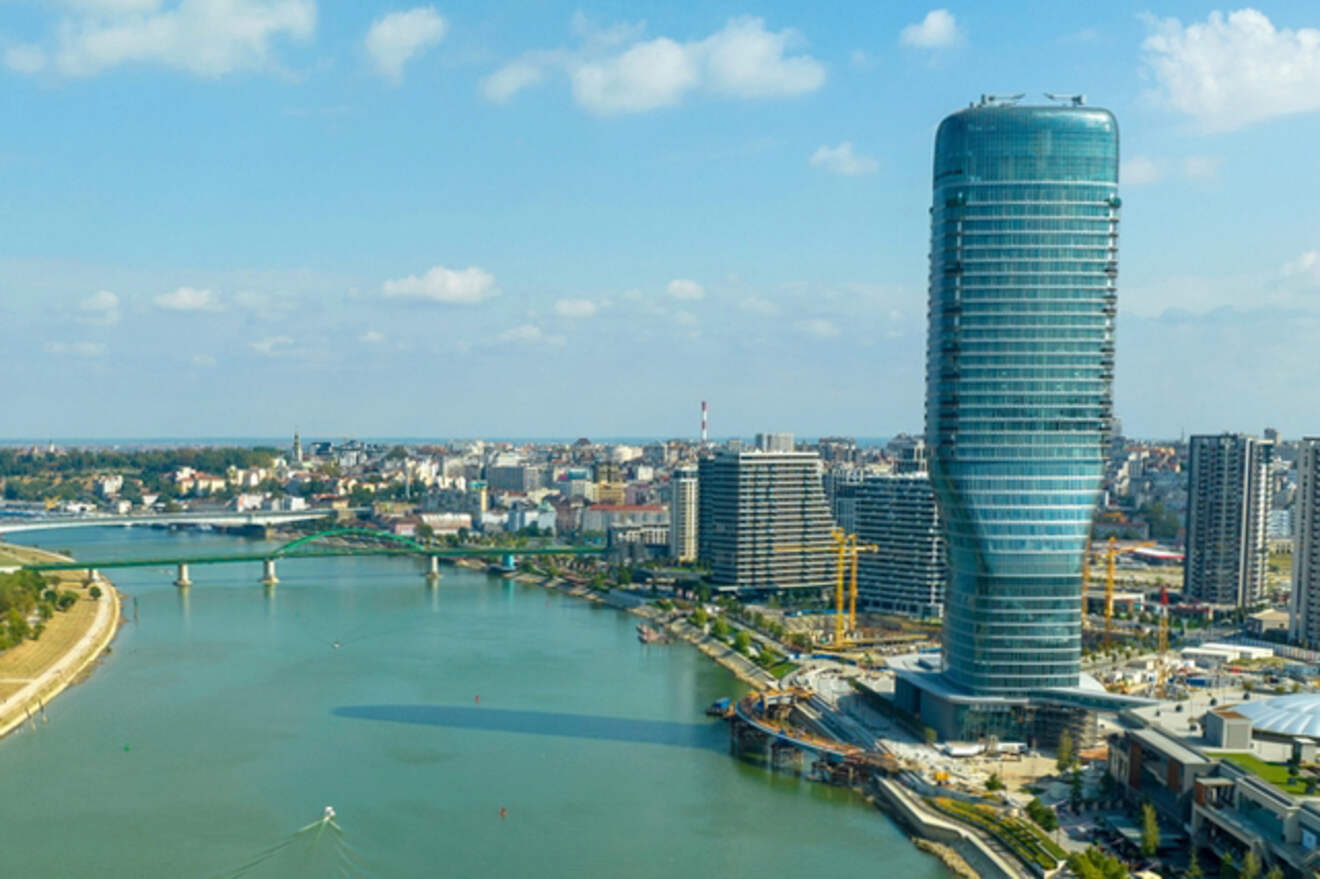 Aerial view of Belgrade with the modern, twisting glass tower of the Belgrade Tower dominating the skyline near the confluence of the Sava and Danube rivers.